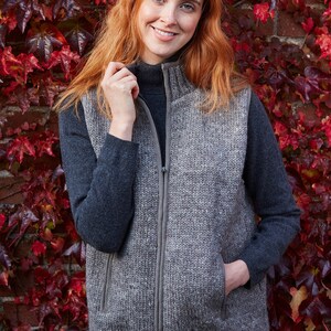 May include: A gray knitted vest with a zipper closure and two pockets. The vest is worn over a black turtleneck shirt and blue jeans.