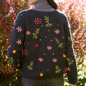May include: A dark gray knitted cardigan with embroidered flowers and leaves in shades of pink, green, and yellow.