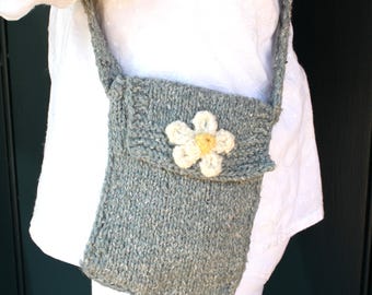 Pode incluir: Uma bolsa transversal de tricô cinza com acabamento em fio texturizado e salpicado e fecho de aba. A parte frontal da bolsa é adornada com uma aplicação de flor branca de crochê com um centro amarelo, fixada no centro da aba.