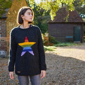 Könnte beinhalten: Ein dunkelgrauer Strickpullover mit einem großen Regenbogen-Stern-Design. Der Pullover hat einen Rundhalsausschnitt und lange Ärmel.