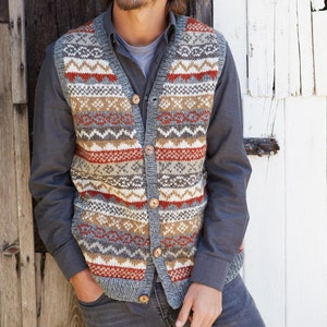以下が含まれることがあります： グレーのニットベストにカラフルな幾何学模様と木製のボタンが付いています。ベストはVネックで、グレーのシャツの上に着ています。
