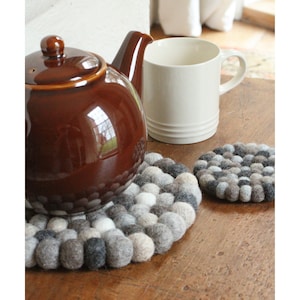 Peut inclure: Deux dessous-de-plat ronds en feutre gris, blanc et noir. Les dessous-de-plat sont faits de boules de laine et sont parfaits pour protéger les surfaces des plats chauds.