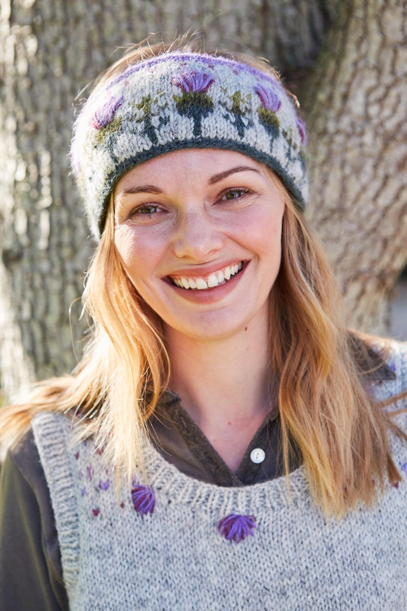 May include: A woman wearing a gray and green knitted headband with purple flowers and a gray knitted vest with purple flower embroidery.