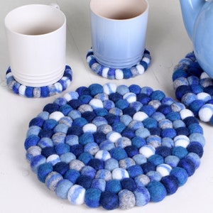 Può includere: Sottobicchieri rotondi in feltro blu, bianco e grigio. I sottobicchieri sono fatti di piccole sfere rotonde di feltro.