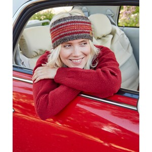 May include: A woman wearing a red sweater and a striped knit headband looks out the window of a red car.