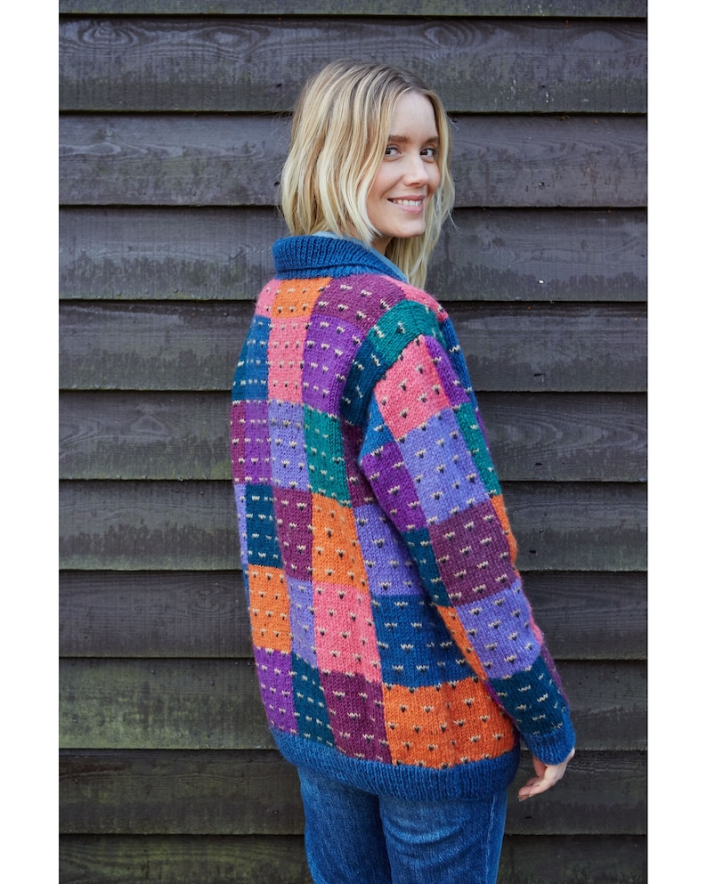 May include: A colorful patchwork cardigan with a blue base and squares of pink, orange, purple, and green. The cardigan is knitted and has a relaxed fit.