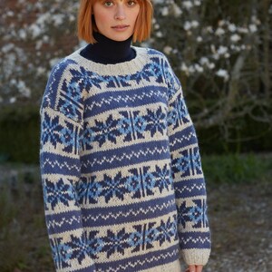 Pode incluir: Um su&eacute;ter de malha azul e branco com um padr&atilde;o de floco de neve. O su&eacute;ter tem gola redonda e mangas compridas.