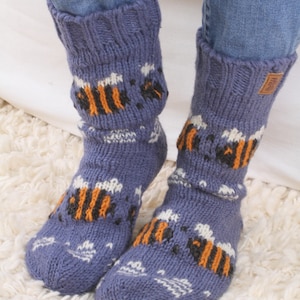 May include: A pair of blue knitted socks with a bee pattern. The socks are folded down at the top and have a white background with orange and black bees.