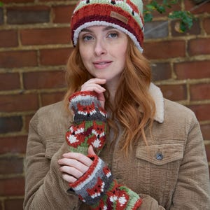 May include: A woman wearing a green, red, and white knit hat with a fox pattern and matching fingerless gloves. The hat has a white pom-pom on top and the gloves have a fox pattern.