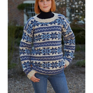 Pode incluir: Um su&eacute;ter de cor creme e azul com gola redonda. O su&eacute;ter tem um design de floco de neve.