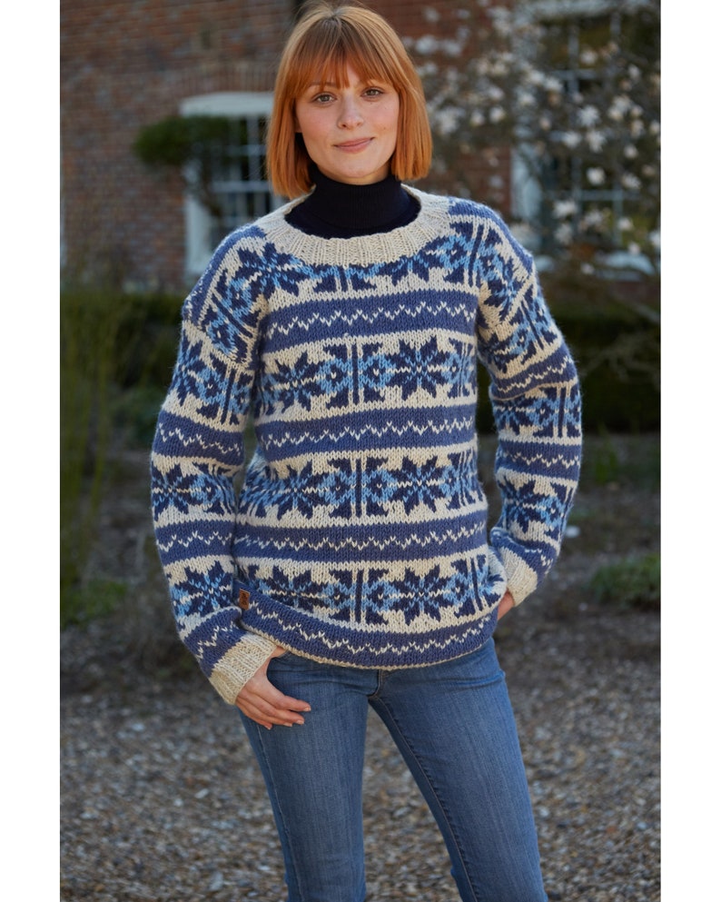 Pode incluir: Um su&eacute;ter de cor creme e azul com gola redonda. O su&eacute;ter tem um design de floco de neve.