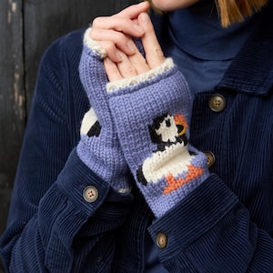 May include: Lavender knitted fingerless gloves with a penguin design. The gloves have a white cuff and a penguin with black, white, and orange details. The person is wearing a navy blue corduroy jacket.