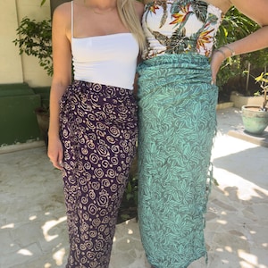 May include: Two women wearing sarongs. One sarong is purple with a swirl pattern and the other is green with a leaf pattern.
