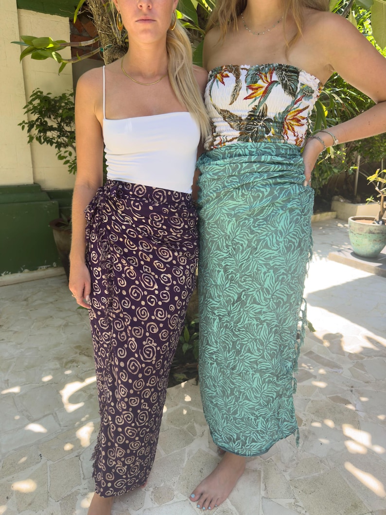 May include: Two women wearing sarongs. One sarong is purple with a swirl pattern and the other is green with a leaf pattern.