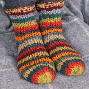 May include: A pair of colorful striped knitted socks with a green, red, orange, yellow, brown, and gray color scheme. The socks are made of a thick, chunky yarn and have a cozy, comfortable look.