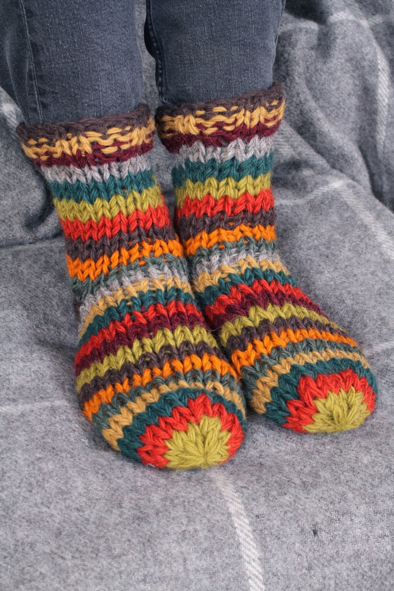 May include: A pair of colorful striped knitted socks with a green, red, orange, yellow, brown, and gray color scheme. The socks are made of a thick, chunky yarn and have a cozy, comfortable look.