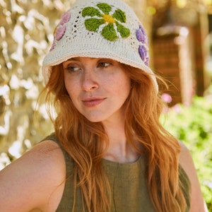 May include: A white crocheted bucket hat with colorful flower embellishments. The hat has a wide brim and is made of a lightweight, breathable material.
