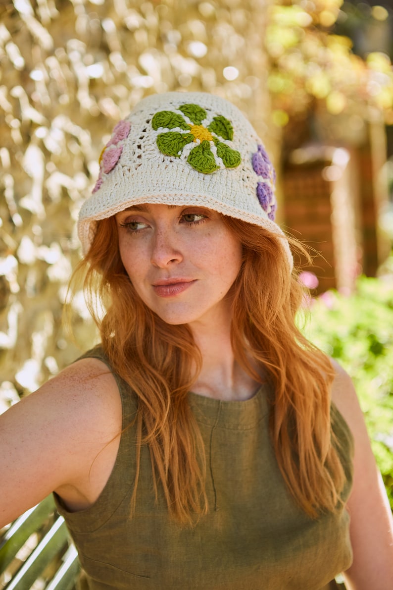May include: A white crocheted bucket hat with colorful flower embellishments. The hat has a wide brim and is made of a lightweight, breathable material.