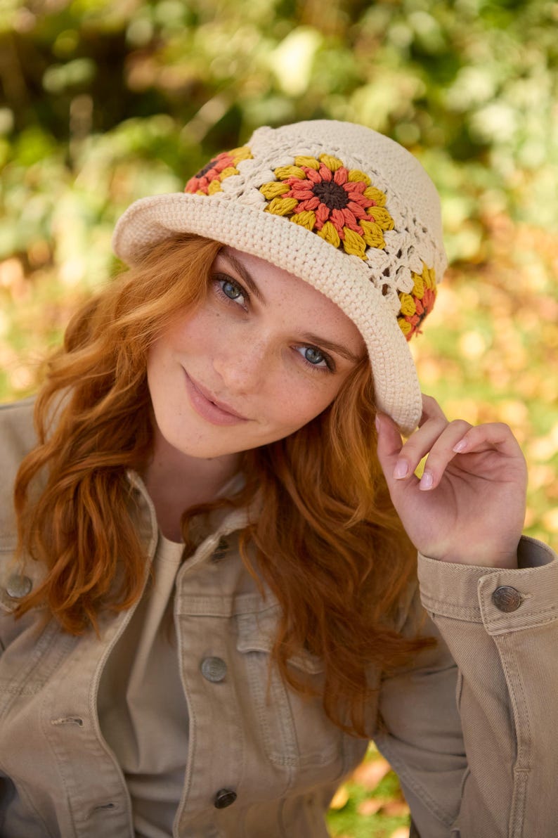 May include: A crocheted hat with a wide brim and a floral design in shades of orange, yellow, and brown. The hat is made with a white yarn and has a crocheted flower pattern around the brim.