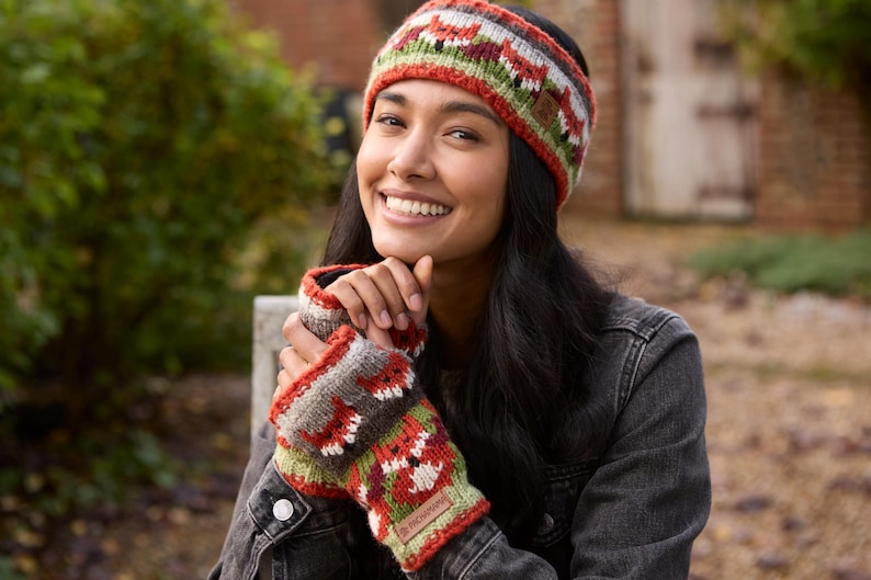 May include: A woman wearing a red, green, and white knit headband with a fox pattern and matching fingerless gloves. The headband and gloves have a brown, gray, and white knit pattern.