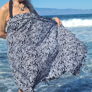 May include: A woman wearing a black and white patterned sarong on a beach. The sarong has a fringed edge and is made of a lightweight fabric.