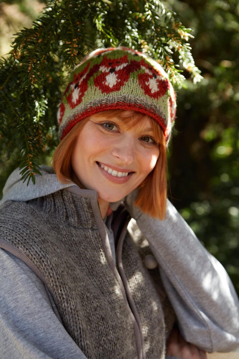 May include: A woman wearing a gray hooded sweater and a red, green, and white knit hat with a fox design. The hat has a red brim and a green and white pattern.