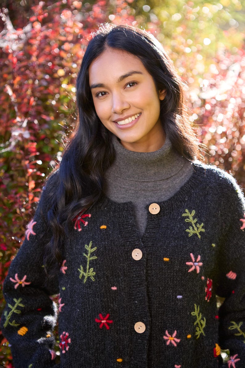 May include: A black knitted cardigan with colorful floral embroidery. The cardigan has a mock neck and button closure.
