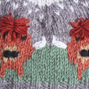 Puede incluir: Un gorro de punto con un patr&oacute;n gris, blanco y verde. Dos alces rojos y naranjas est&aacute;n bordados en el gorro.