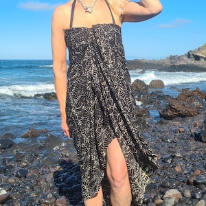 May include: A black and white patterned wrap dress with a halter neckline. The dress is worn by a person standing on a rocky beach.