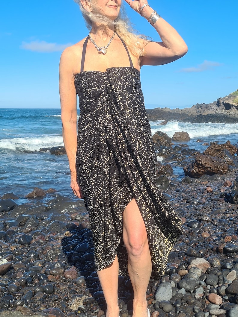 May include: A black and white patterned wrap dress with a halter neckline. The dress is worn by a person standing on a rocky beach.