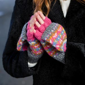 Op de afbeelding: Een paar roze en grijze vingerloze handschoenen met een kleurrijk geometrisch patroon. De handschoenen zijn gebreid en hebben een zacht, comfortabel gevoel.
