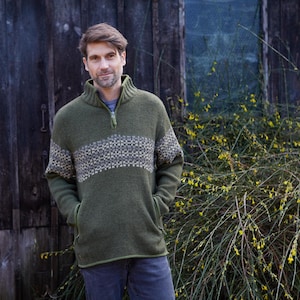 May include: A green knitted sweater with a white and gray patterned band across the chest. The sweater has a zipper at the neck and two pockets.