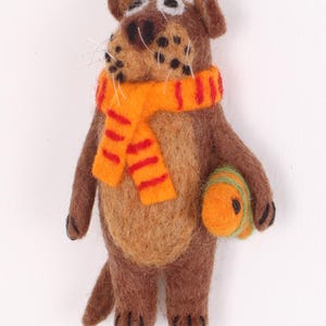 May include: A brown felt animal ornament with a striped orange and red scarf and a green and orange felt ball. The ornament has a string for hanging.