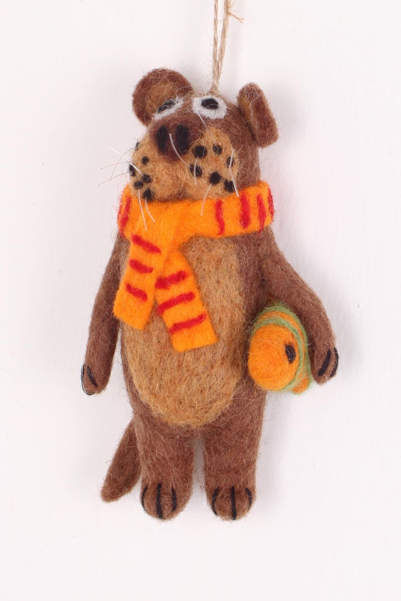 May include: A brown felt animal ornament with a striped orange and red scarf and a green and orange felt ball. The ornament has a string for hanging.