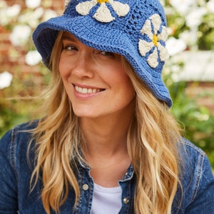 May include: A blue crochet bucket hat with white daisy appliques. The hat has a yellow center on each daisy.