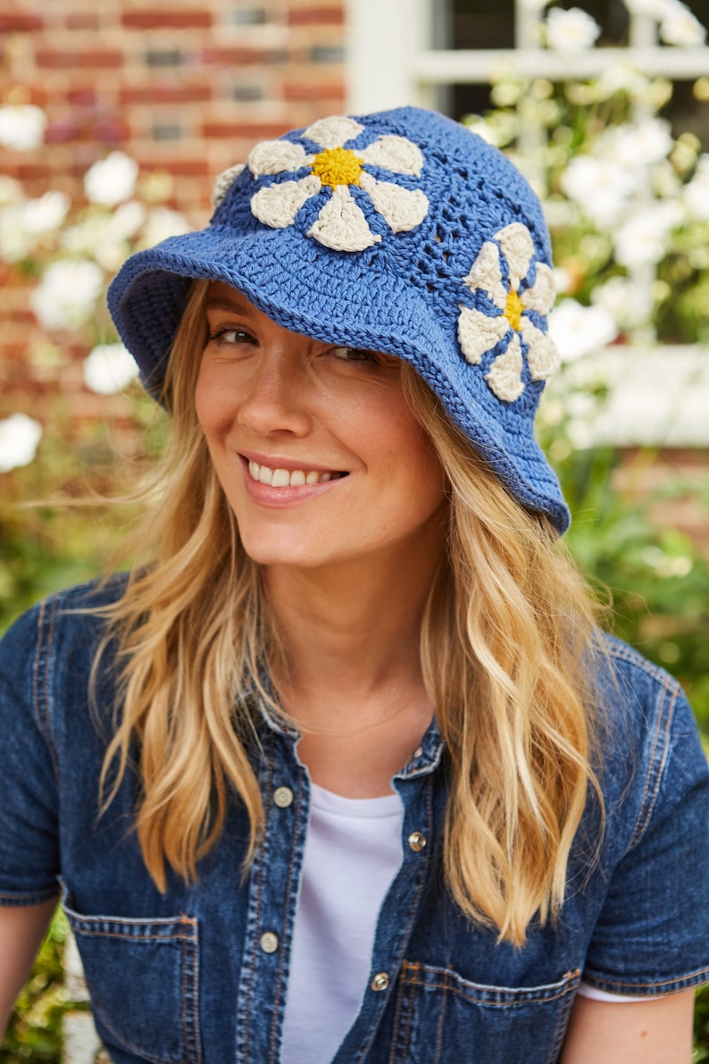 May include: A blue crochet bucket hat with white daisy appliques. The hat has a yellow center on each daisy.