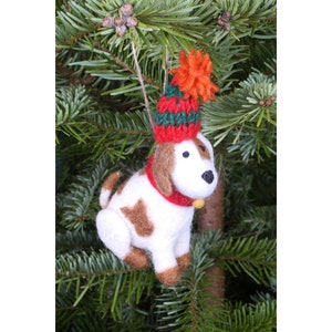 Könnte beinhalten: Weißer und brauner Filz-Hunde-Anhänger mit einer rot-grünen Strickmütze mit einem flauschigen orangefarbenen Bommel.