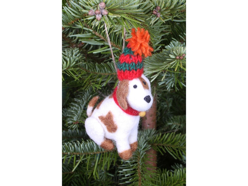 May include: White and brown felt dog ornament wearing a red and green knit hat with a fuzzy orange pom pom.