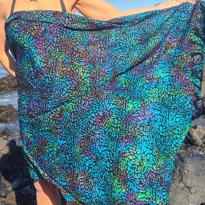 May include: A blue and black sarong with a floral pattern. The sarong is made of a lightweight fabric and has a fringed edge.