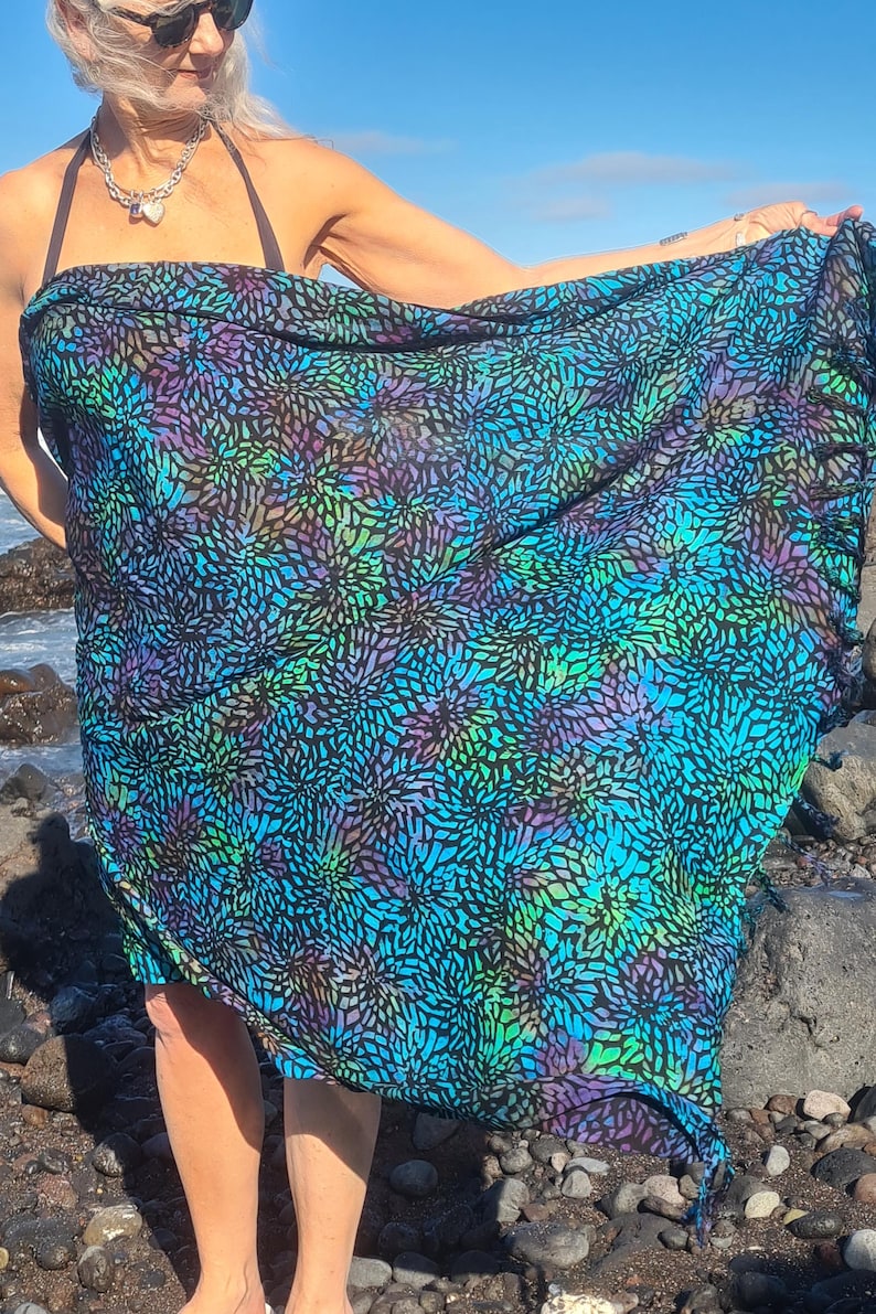 May include: A blue and black sarong with a floral pattern. The sarong is made of a lightweight fabric and has a fringed edge.