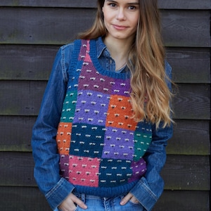 Op de afbeelding: Een vrouw draagt een kleurrijk patchwork gebreid vest met een spijkerjack en jeans.