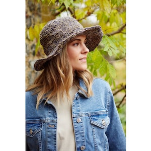 May include: A woman wearing a blue denim jacket and a brown and blue crocheted sun hat. The hat has a wide brim and a textured design.