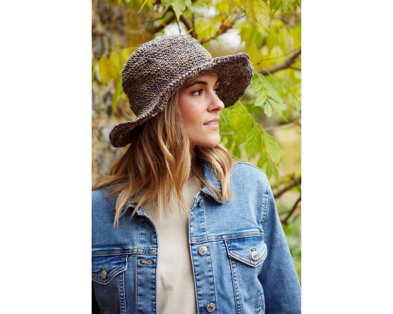May include: A woman wearing a blue denim jacket and a brown and blue crocheted sun hat. The hat has a wide brim and a textured design.