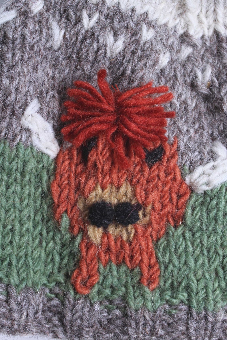 Puede incluir: Un gorro de punto con un dise&ntilde;o rojo, marr&oacute;n y verde. El gorro presenta una imagen de punto de un zorro con una cola tupida.