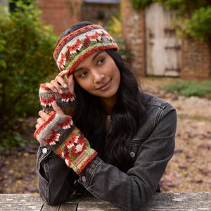 May include: A woman wearing a colorful knitted headband and matching fingerless gloves. The headband and gloves feature a geometric pattern with red, orange, green, and gray colors.