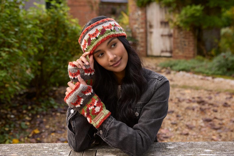 May include: A woman wearing a colorful knitted headband and matching fingerless gloves. The headband and gloves feature a geometric pattern with red, orange, green, and gray colors.