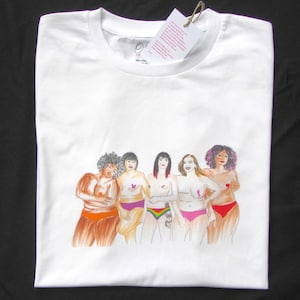 Puede incluir: Camiseta blanca con un gr&aacute;fico de cinco mujeres de pie juntas, cada una con un peinado y un tipo de cuerpo diferente. Las mujeres llevan ropa interior de varios colores y tienen cintas rosas en el pecho. El texto "100% Algod&oacute;n" est&aacute; impreso en la camiseta.