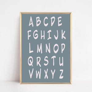 May include: A framed alphabet print. The letters A through Z are displayed in a white, handwritten font against a muted teal background. The frame is gold. The print is a decorative piece for a nursery or child's room.