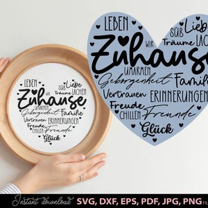 May include: A wooden framed wall art piece with the word "Zuhause" in the center, surrounded by other words in German. A blue heart-shaped graphic with the same text is also visible. The words are in a black script font.