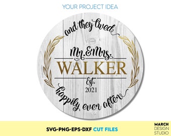 May include: A white wooden round sign with a gold wreath design and black calligraphy text that reads "and they lived happily ever after" with the text "My & Mrs. WALKER Est. 2021" in the center.